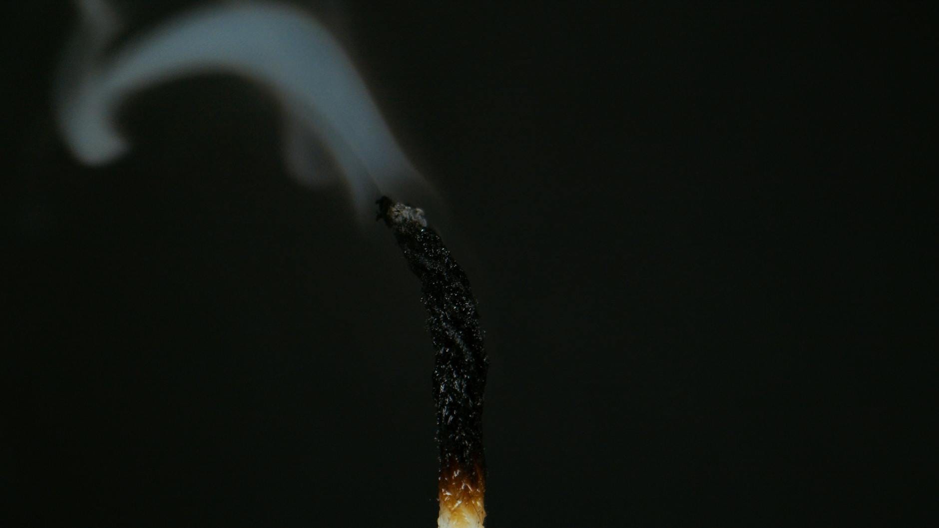 Zbliżenie spalonego knota świecy z unoszącym się dymem na ciemnym tle