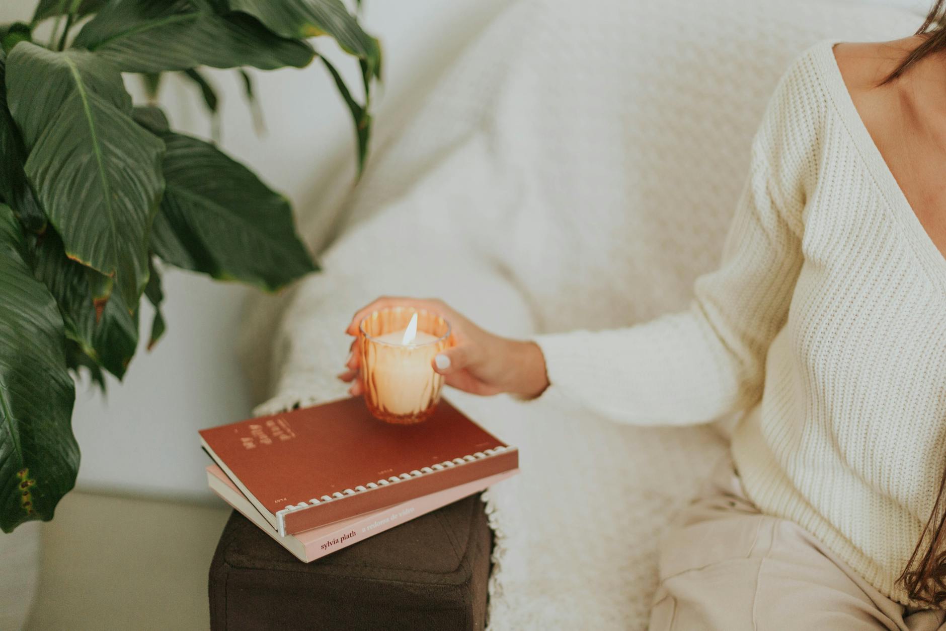 Kobieta trzyma zapaloną świecę w przytulnym salonie obok książek i rośliny