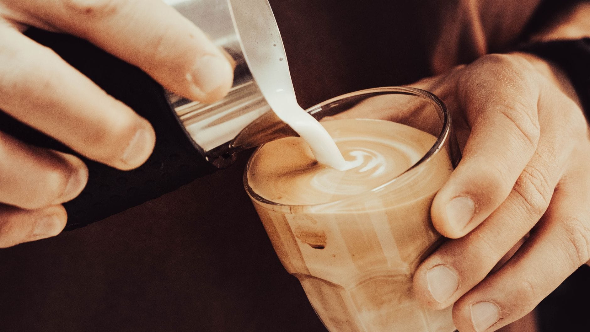 Barista wlewa mleko do filiżanki, tworząc wzór na cappuccino Barista wlewa mleko do filiżanki, tworząc wzór na cappuccino